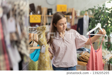 Positive teenage girl choosing something for summer in clothing store 139205205