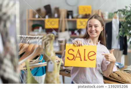 Teenage girl holding sale banner in clothing store Teenage girl holding sale banner in clothing store 139205206