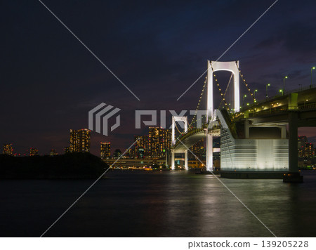 The illuminated Rainbow Bridge and the cityscape, with white light reflecting on the water's surface (Odaiba, Minato Ward, Tokyo) 139205228