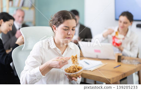 Young beautiful businesswoman having takeout meal during lunch break at work sitting at workplace at laptop with other colleagues in office Young beautiful businesswoman having takeout meal during lunch break at work sitting at workplace at laptop with other colleagues in office 139205233