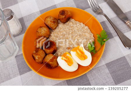 Soft-boiled eggs, golden meatballs and oatmeal on orange plate 139205277