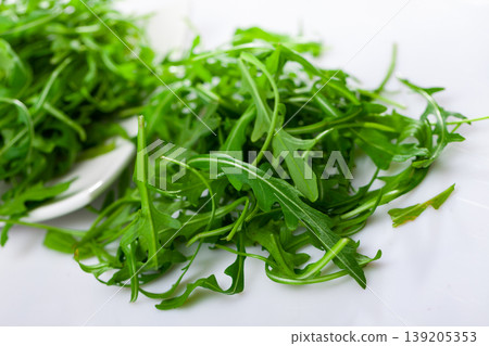 On white background there is white ceramic plate with pile of fresh arugula leaves. 139205353