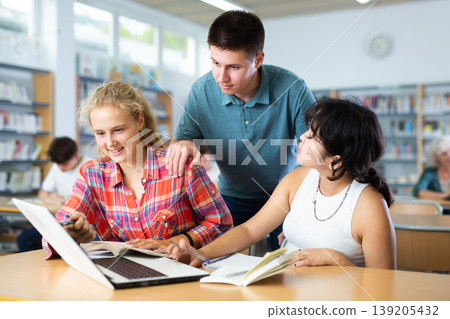 Three schoolchildren are studies on a laptop and taking abstracts in a copybook Three schoolchildren are studies on a laptop and taking abstracts in a copybook 139205432