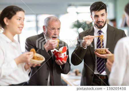 Group of colleagues, man and woman, are having lunch in office during their break, eating noodles Group of colleagues, man and woman, are having lunch in office during their break, eating noodles 139205438