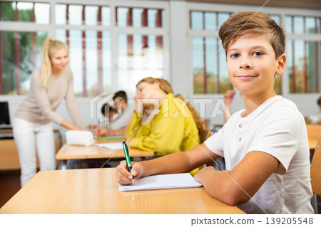 Boy listening to lecturer and writing in notebook in classroom Boy listening to lecturer and writing in notebook in classroom 139205548