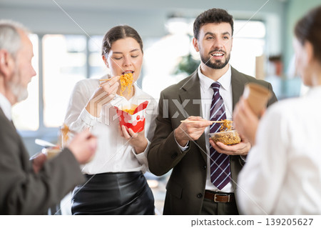 Group of friendly young office workers different ages standing and eating fast food at modern office canteen 139205627
