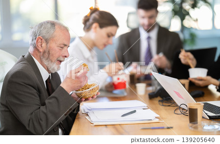 Lunch break - mature man eating noodles with colleagues in modern office Lunch break - mature man eating noodles with colleagues in modern office 139205640