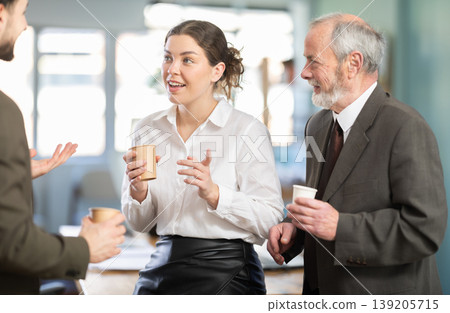Coffee break - men and young woman drink coffee and chat lively with each other in modern office 139205715