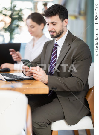 Man scrolls feed and passes time on social media. Bored staff on smartphone in background 139205758