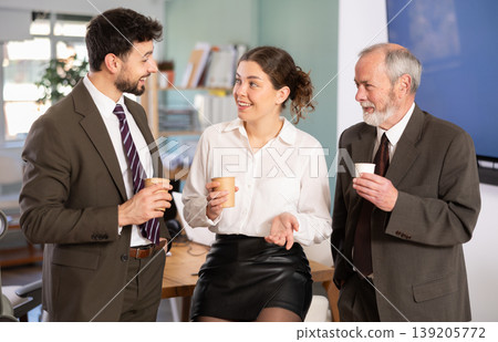 Young woman and two man co-worker drinking coffee and friendly talking during break while working in office Young woman and two man co-worker drinking coffee and friendly talking during break while working in office 139205772