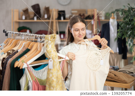 Girl chooses a set of clothes for summer. Visitor to the boutique examines the new summer collection of clothes Girl chooses a set of clothes for summer. Visitor to the boutique examines the new summer collection of clothes 139205774