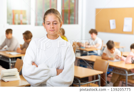 Upset girl stands in a school class against background of classmates Upset girl stands in a school class against background of classmates 139205775