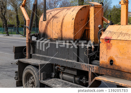 An asphalt laying machine is parked on the road, showing its machinery and tool setup in an urban location under bright daylight 139205783