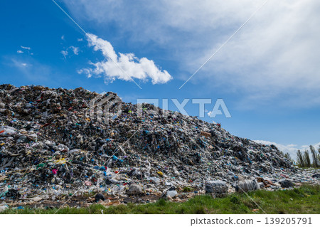 A large garbage dump is seen with heaps of waste under a blue sky, illustrating pollution challenges near a city 139205791