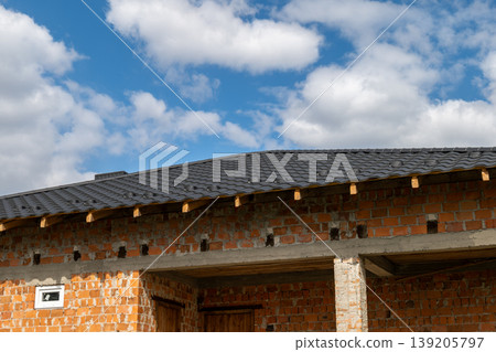 Roof installation takes place on a building with a metal tile roof, showcasing an ongoing construction process and blue sky above Roof installation takes place on a building with a metal tile roof, showcasing an ongoing construction process and blue sky above 139205797