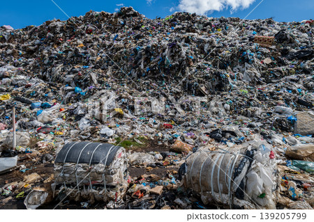 A large heap of waste is present at a municipal garbage dump with trash bags and plastic scattered across the ground during daylight 139205799