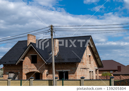 New modern house stands in a residential area. The construction shows a black roof against a clear blue sky 139205804