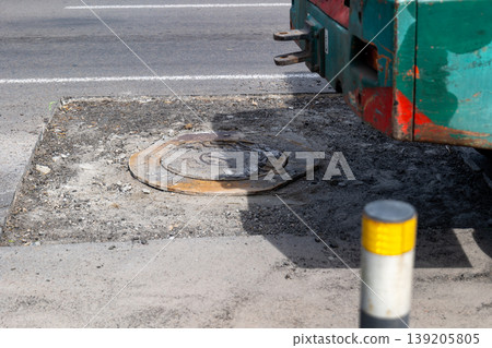 Workers are engaged in road works by laying asphalt next to a manhole cover on a busy city street during daylight hours Workers are engaged in road works by laying asphalt next to a manhole cover on a busy city street during daylight hours 139205805