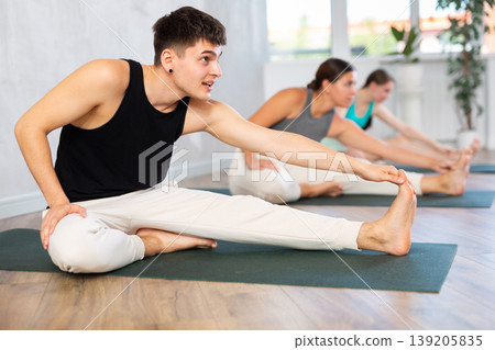 Young man practicing head to knee pose of yoga in light fitness room 139205835