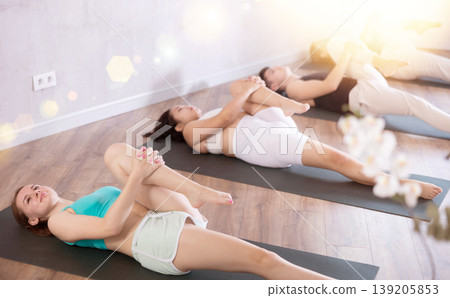 Groupd og young people doing reclining twist yoga pose in studio. Groupd og young people doing reclining twist yoga pose in studio. 139205853