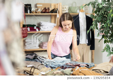 Positive teenage girl choosing pantaloon in clothing store Positive teenage girl choosing pantaloon in clothing store 139205854