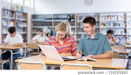 Teenage students help each other study at laptop while sitting in school library Teenage students help each other study at laptop while sitting in school library 139205891