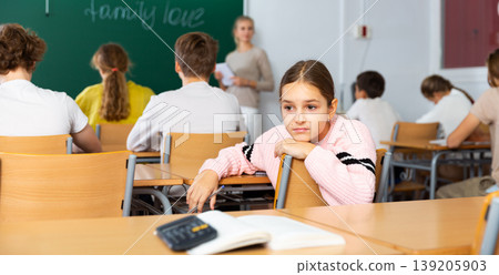 Sad young schoolgirl sitting at desk during lesson 139205903