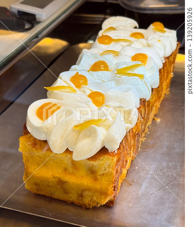 Rectangular sponge cake topped with whipped cream and fruit jelly decorations. Bakery product display, dessert preparation, pastry craft, and confectionery presentation. Rectangular sponge cake topped with whipped cream and fruit jelly decorations. Bakery product display, dessert preparation, pastry craft, and confectionery presentation. 139205926