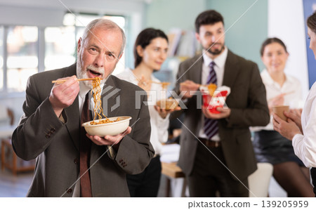 Mature businessman having takeout meal during lunch break at work with other colleagues in office Mature businessman having takeout meal during lunch break at work with other colleagues in office 139205959