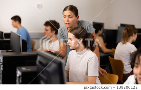 Focused female student explaining the topic to female friend while she is studying computer science on the pc in the classroom Focused female student explaining the topic to female friend while she is studying computer science on the pc in the classroom 139206122