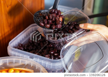 Woman buying marinated black olives with pits at farmers market; putting olives in container Woman buying marinated black olives with pits at farmers market; putting olives in container 139206126