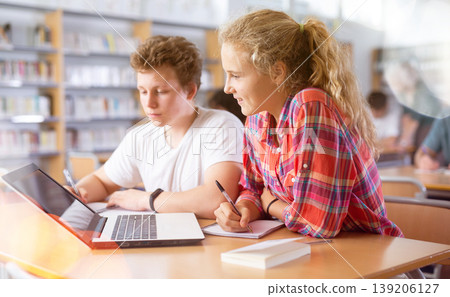 Teenage students help each other study at laptop while sitting in school library 139206127