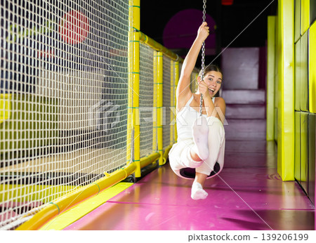 Laughing girl enjoying swing ride on zipline at indoor entertainment venue 139206199