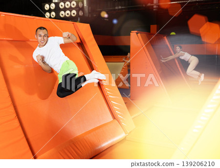 Excited man pushing off from inclined surface in indoor trampoline center Excited man pushing off from inclined surface in indoor trampoline center 139206210