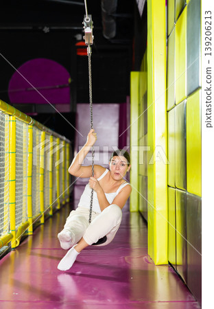 Cheerful young girl riding zip line in indoor amusement center 139206213