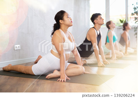Young people doing pigeon yoga pose in class. 139206224