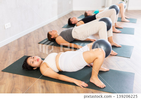 Young fitness woman and man in activewear working out with soft ball pilates on mat while doing upper body training in crossfit class Young fitness woman and man in activewear working out with soft ball pilates on mat while doing upper body training in crossfit class 139206225