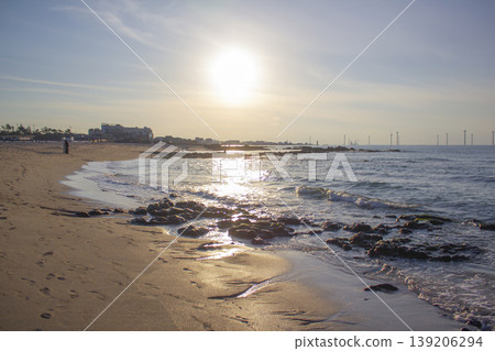 It is a beach scene with the sun setting. 139206294