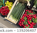 Fresh radishes, scallions, peppers and leafy greens displayed in crates outside a shop. Vegetable retail, seasonal produce, grocery shopping and local food market freshness. 139206407
