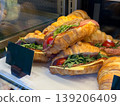 Croissant sandwiches with cheese, salami, and arugula in display case. Bakery assortment, ready food choice, snack purchase, and cafe offering with layered ingredients. 139206409