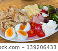 Assorted breakfast plate with eggs, tomato, cheese, ham, salad, radish, cream and grilled bread on a wooden table. Balanced brunch, cafe meal, protein, dairy, vegetable and bakery serving. 139206433