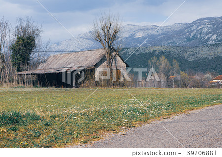 Old Barn in Spring Countryside With Meadow Wildflowers and Mountain Backdrop Under Cloudy Sky 139206881
