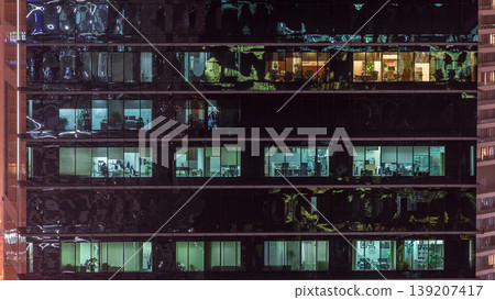 Office skyscraper exterior during late evening with interior lights on and people working inside night timelapse Office skyscraper exterior during late evening with interior lights on and people working inside night timelapse 139207417