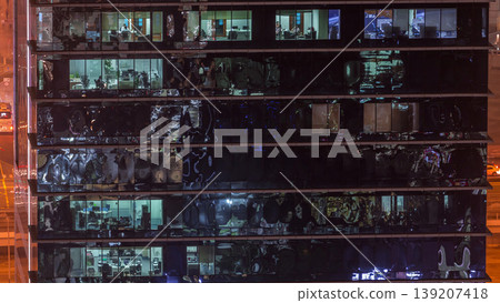 Office skyscraper exterior during late evening with interior lights on and people working inside night timelapse Office skyscraper exterior during late evening with interior lights on and people working inside night timelapse 139207418