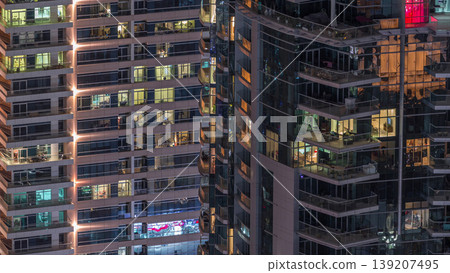 Rows of glowing windows with people in apartment building at night. 139207495