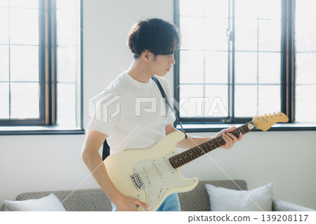 一位年輕男子在沙發上彈吉他。 一位年輕男子在沙發上彈吉他。 139208117