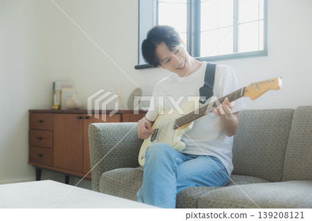 A young man playing the guitar on a sofa. A young man playing the guitar on a sofa. 139208121