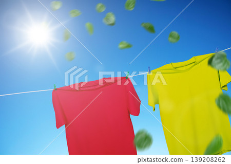 Vibrant red and yellow t-shirts hanging on a clothesline against a clear blue sky. Bright sun shines as fresh green leaves blow in the wind, representing freshness and clean laundry Vibrant red and yellow t-shirts hanging on a clothesline against a clear blue sky. Bright sun shines as fresh green leaves blow in the wind, representing freshness and clean laundry 139208262