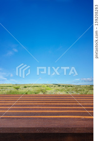 A weathered table top surface serving as a platform in front of a vast green savanna under a bright clear blue sky. Perfect for outdoor product mockups 139208263