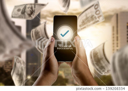 Hands holding a smartphone showing a successful transfer notification with US dollar bills flying in the background. Conceptual image for mobile banking and fintech Hands holding a smartphone showing a successful transfer notification with US dollar bills flying in the background. Conceptual image for mobile banking and fintech 139208334